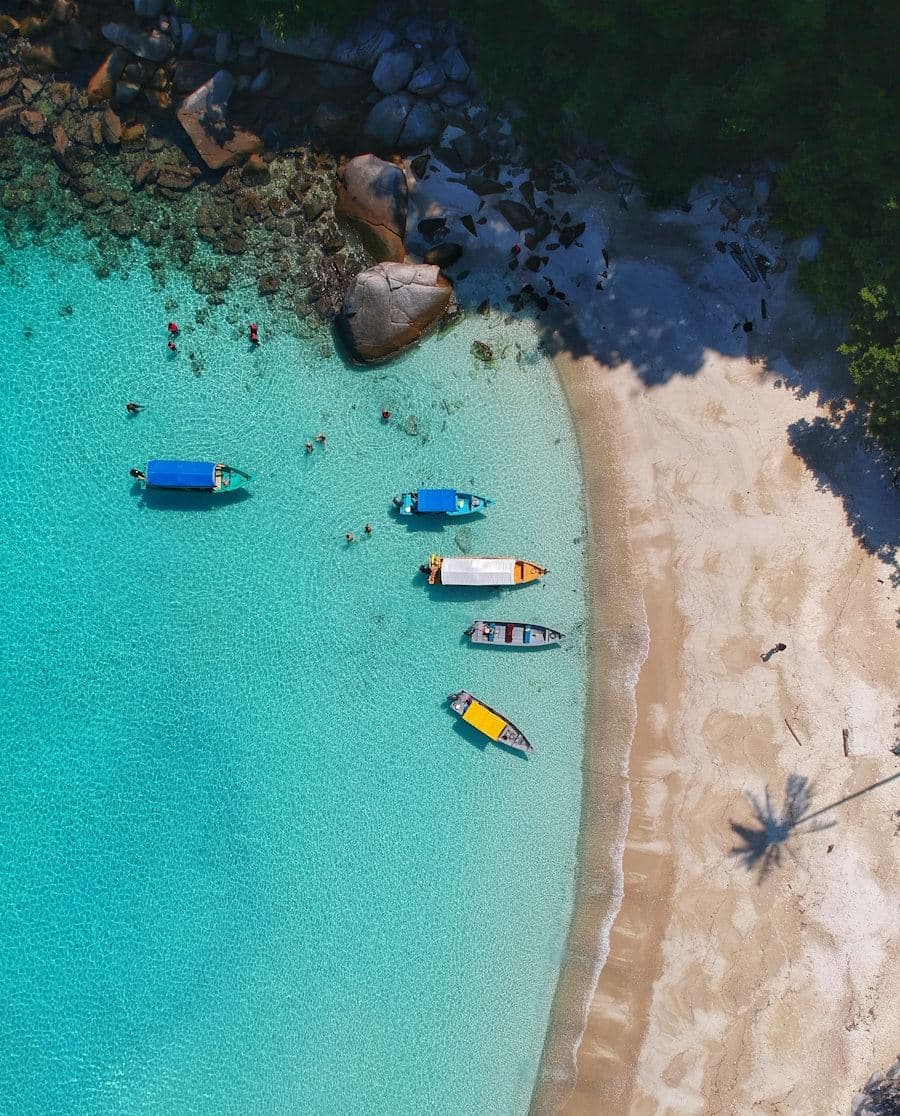 Aerial view of boats moored on clear turquoise water beside a quiet sandy beach